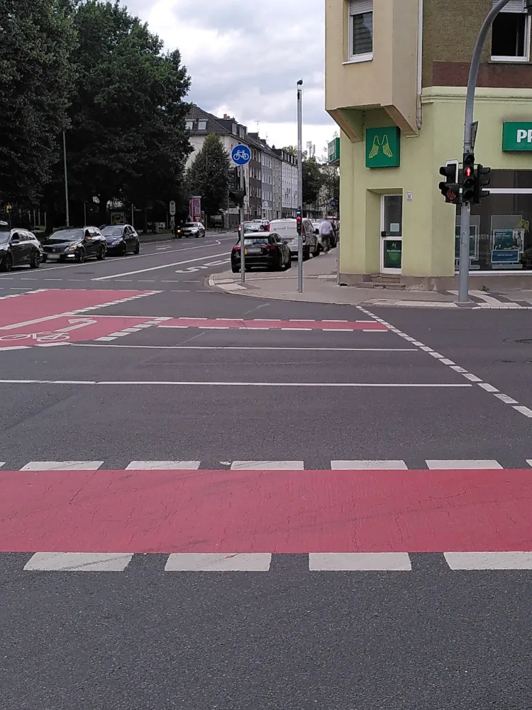 Ein Fußgängerüberweg an einer Kreuzung. In der Mitte des Bildes, auf der gegenüberliegenden Straßenseite, steht eine Fahrradampel.
