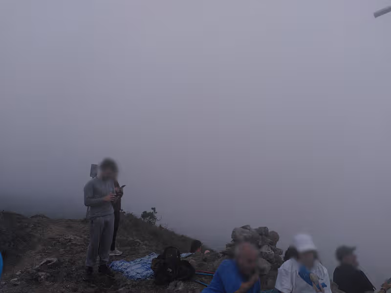 Im Vordergrund mehrere Menschen, die auf einem spärlich bewachsenen Untergrund stehen. Es ist dichter Nebel, man kann nicht weit sehen.