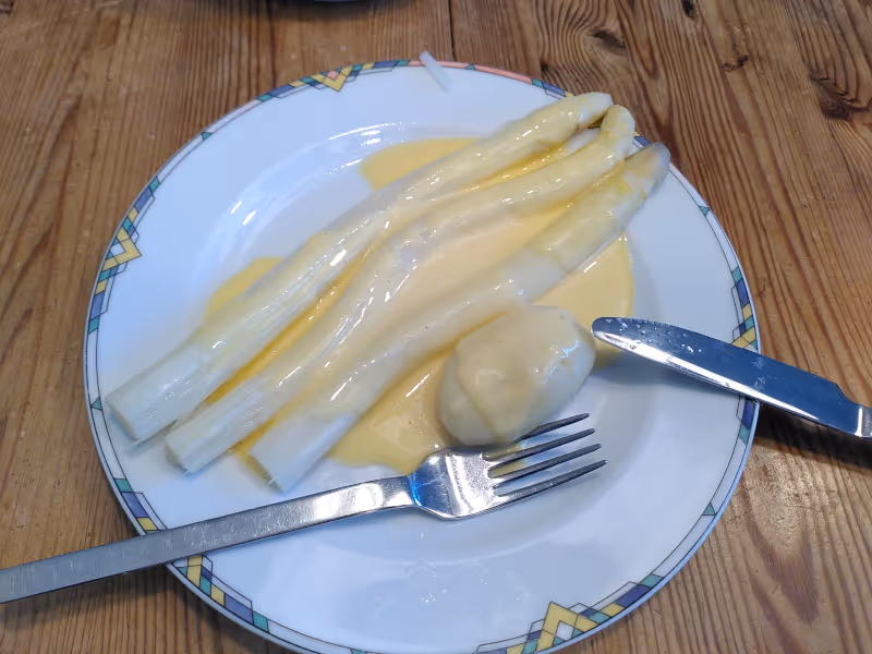 Ein Teller, auf dem drei Stangen Spargel und eine kleine Kartoffel liegen, mit einer Soße bedeckt.