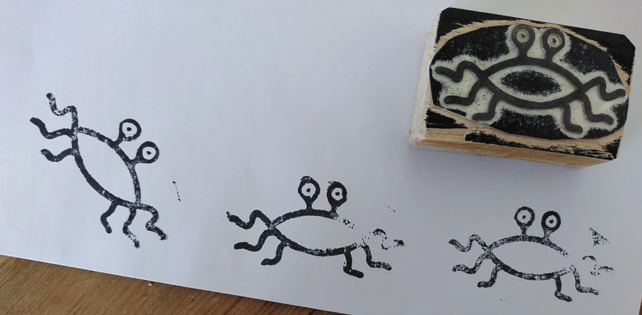 Drei Stempelabdrücke des fliegenden Spaghettimonsters in schwarzer Farbe auf weißem Papier. Daneben mit dem Motiv nach oben der dazugehörige Stempel