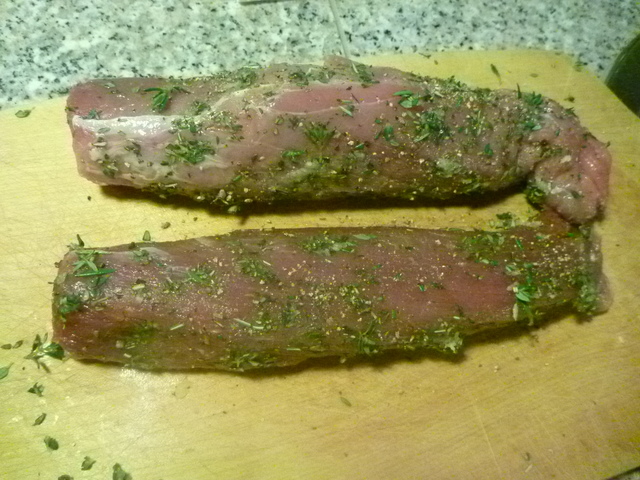 zwei rohe Schweinefilets, rundherum mit Kräutern und Pfeffer bedeckt