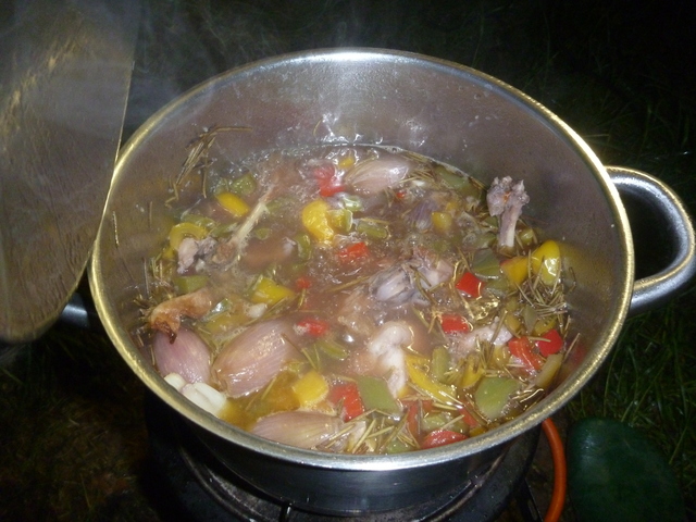 In einem Edelstahltop ist eine Brühe in der Gemüse und Rosmarin schwimmt. Hier und da schaut ein Stückchen Fleisch heraus