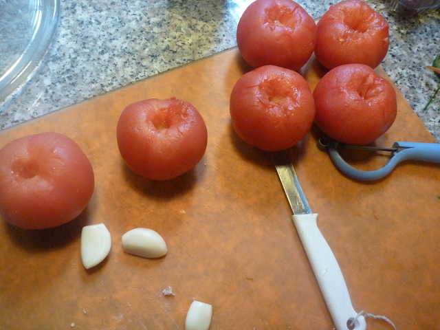 geschälte Tomaten und Knoblauchzehen auf einem Schneidebrett