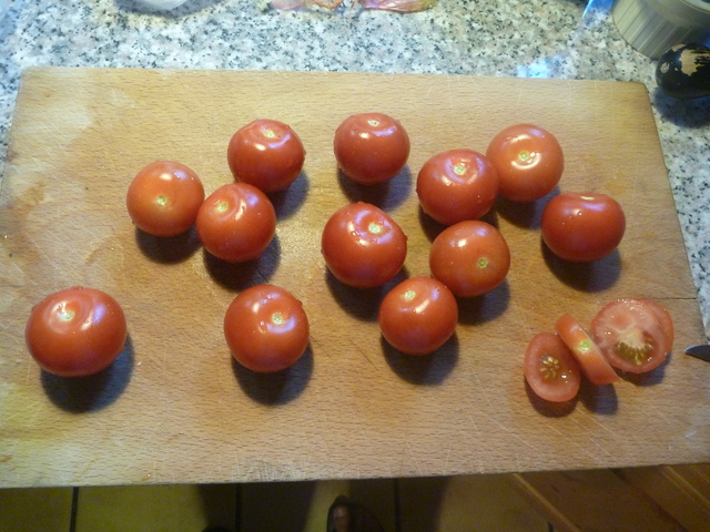 13 Tomaten auf einem Schneidebrett, eine davon ist in Scheiben geschnitten