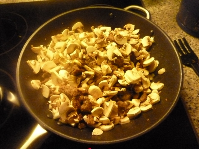 Kleingeschnittene Champignons auf Fleisch in einer Pfanne