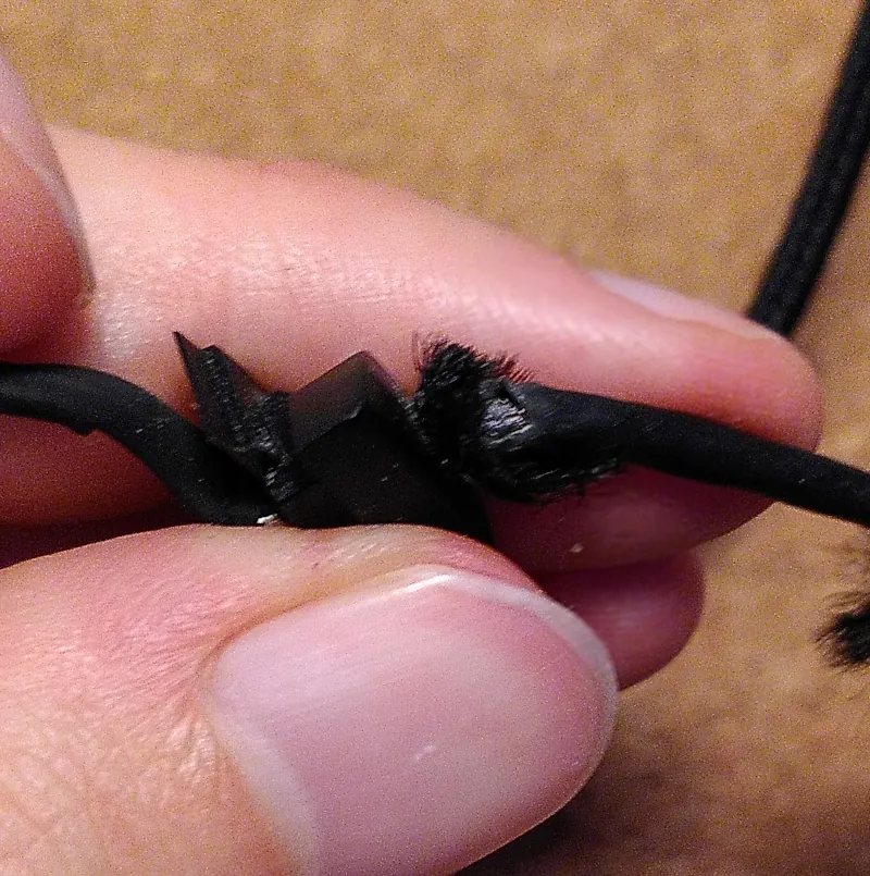 Nahaufnahme von einem schwarzen Mauskabel, gehalten von mehreren Fingern. In der Mitte ist die Isolierung des Kabels aufgebrochen.