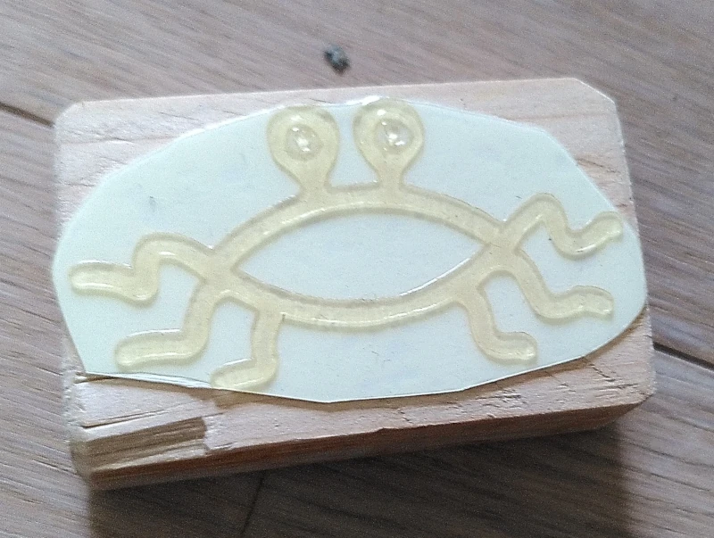 Stempel mit fliegendes-Spaghettimonster-Motiv, mit der Stempelfläche nach oben. Es ist noch keine Farbe am Stempel.